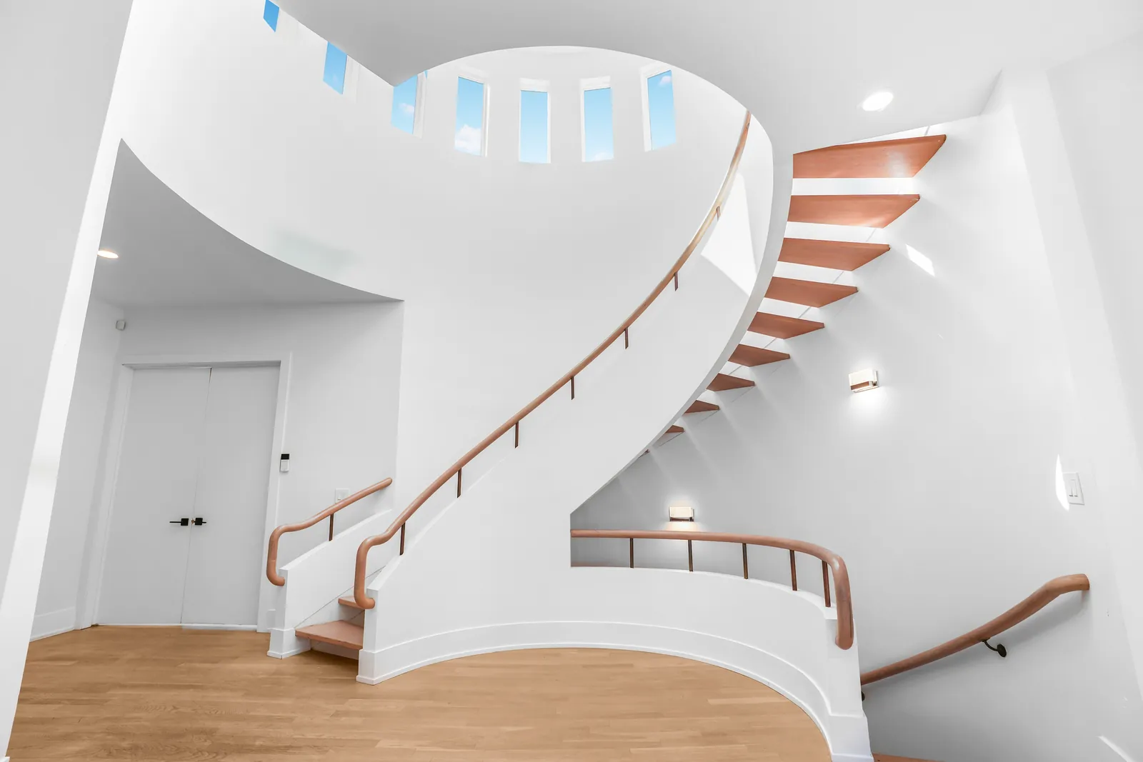 Spiral stair rising through a white stairwell under a ring of skylights