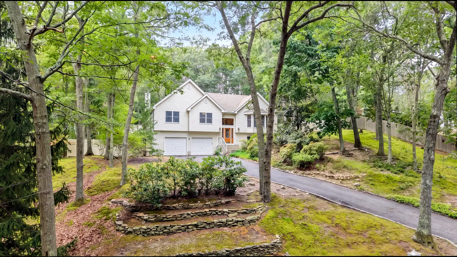 Drone view of the house set back among tall trees, with a curving drive and stone-walled garden beds