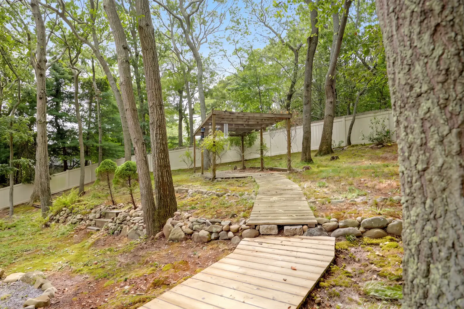 Wood boardwalk path winding through the trees to a pergola in the back yard