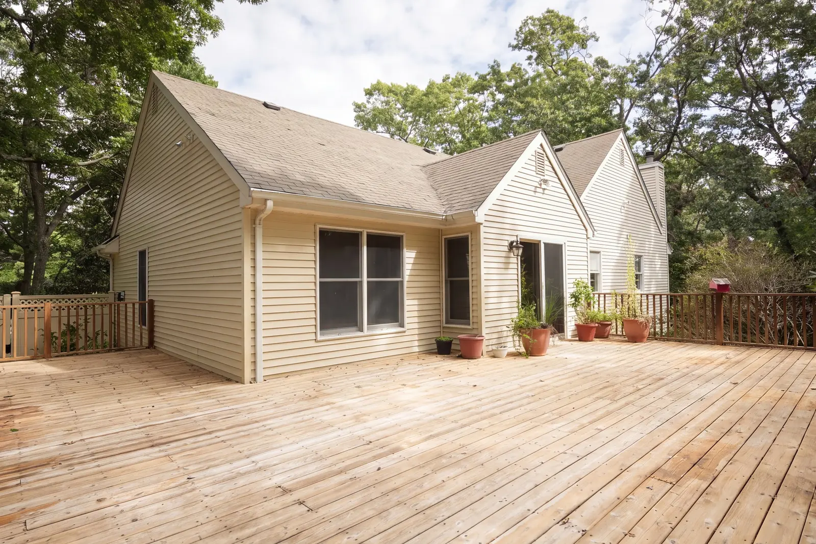 Rear deck of wide wood boards along the back of the house, with trees behind