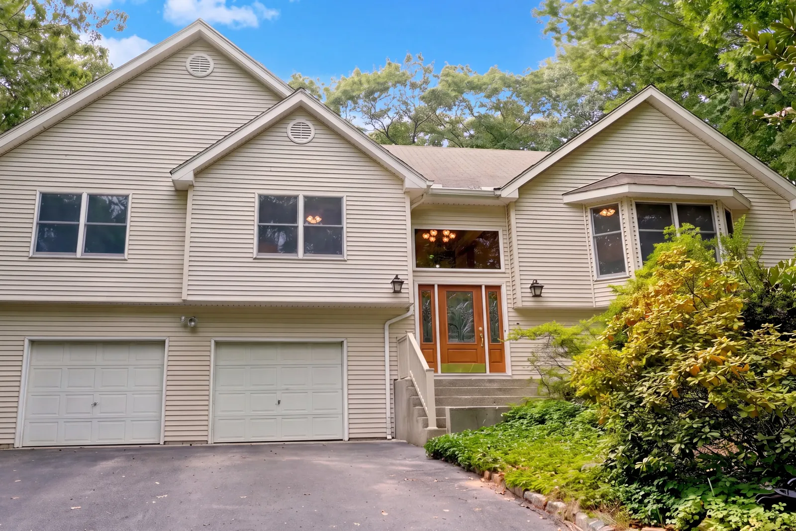 Front of 247 Dogwood Drive in Wading River, with tan siding, garage doors at the drive, and steps up to a wood front door