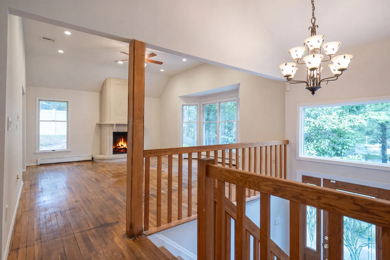 Great room with wood floors, a fireplace, a bay window, and a wood railing over the stair to the front door