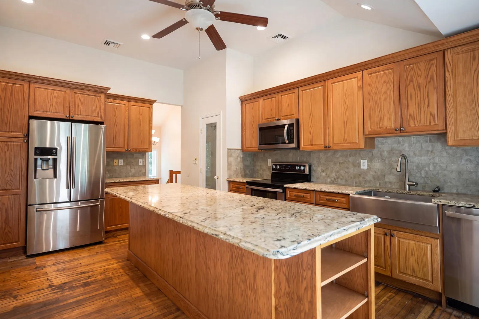 Kitchen with wood cabinets, a granite island, a farmhouse sink, and stainless appliances
